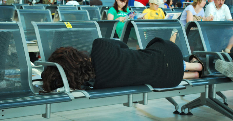 A tired passenger sleeping on an airport terminal bench in Copenhagen, Denmark